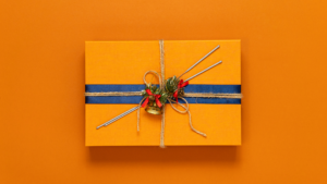 An box wrapped in orange wrapping paper with a navy blue ribbon and twine tied around it. The background is also orange.